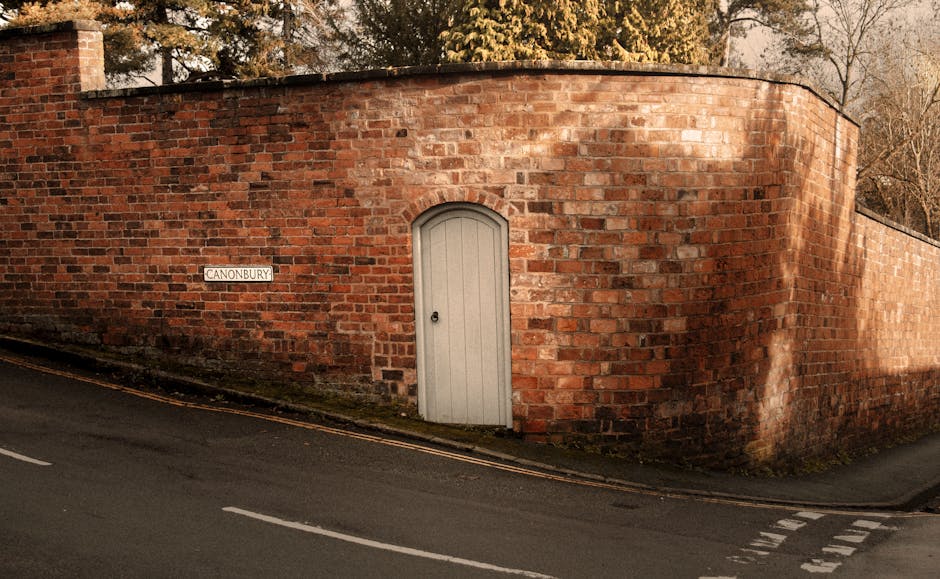 Photograph of a narrow residential alleyway with brick walls on either side, lined with school pavement stones. On the left side, there is a green wheelie bin placed near the base of a brick wall that