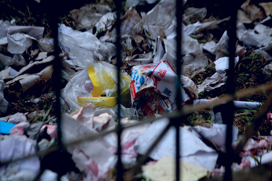 A close-up of a person dressed in orange work clothing and wearing a white glove, holding a large blue plastic bag filled with waste material during a house removal or relocation process. The person i